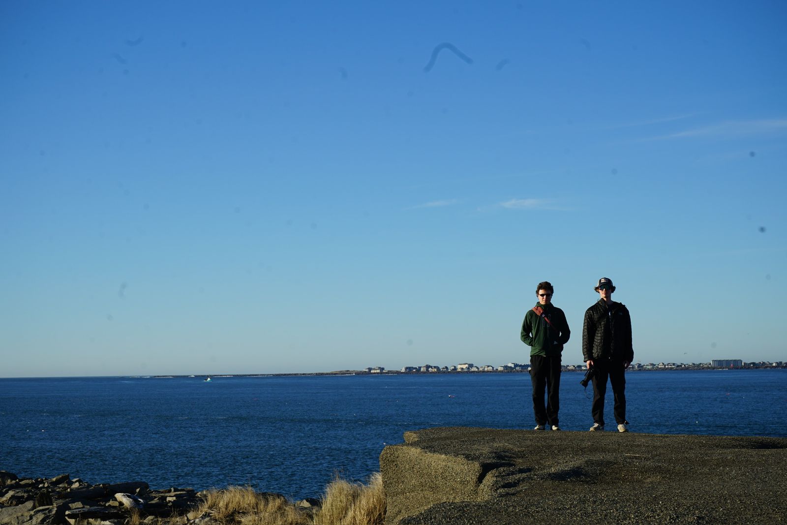 Two people on a concrete platform beside blue water, Westport